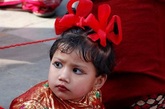 尼泊尔，加德满都湿婆神庙广场上热闹非凡，绳子围起的场地中坐满了装扮华丽的小女孩，身边还有母亲等家人陪伴。对面的庙前则拉着写着尼泊尔语的横幅。这就是尼泊尔的贝尔果婚礼大典。