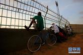 8月16日，在塞内加尔首都达喀尔市中心的足球场外，一个球迷坐在自行车上观看比赛。新华社记者 刘宇摄