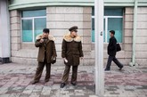 两个朝鲜士兵站在大街上抽烟，边上有两个路人经过。