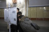 在地铁站内的一个报纸阅读板，人们弓着背，争相看呀看报纸。