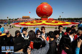 游客在天安门广场花坛前留影。国庆节当日，来自祖国各地的游客来到北京天安门广场参观，感受国庆节带来的喜悦。 新华社发（李方宇 摄）